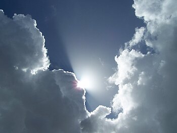 Die Sonne scheint zwischen den Wolken hervor, dahinter tiefblauer Himmel