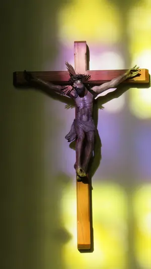 Holzkruzifix, darauf scheint das Sonnenlicht durch gelbe und violette Glasfenster