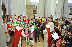 Familiengottesdienst: zahlreiche Kinder bauen mit den Ministrantinnen und dem Pfarrer im Altarraum ein himmlisches Jerusalem aus bunten Kartonziegeln. Auf manchen Ziegeln stehen die Namen der Apostel und die der getauften Kinder im vergangenen Jahr.